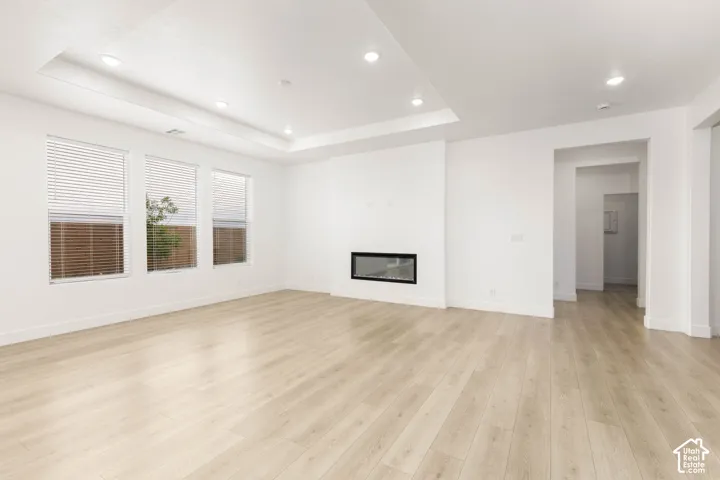 Spacious room featuring wood-finish flooring, a recessed ceiling with integrated lighting, a modern built-in fireplace, and multiple windows with blinds