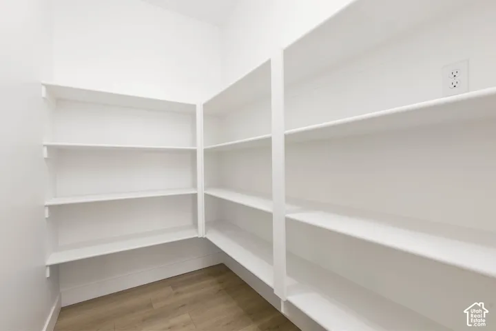 Walk-in pantry with extensive built-in shelving, light wood-finish flooring, and white walls