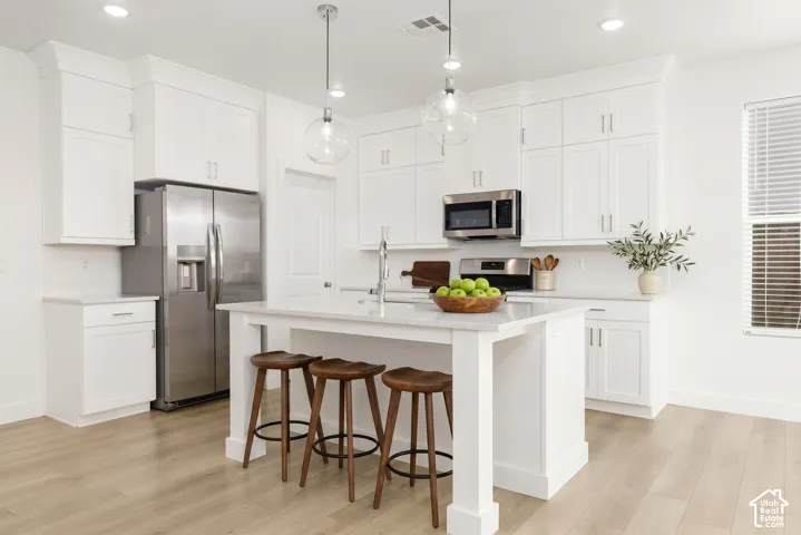 White shaker cabinetry, stainless steel appliances, wood-finish flooring, recessed lighting, and a kitchen island with pendant lighting