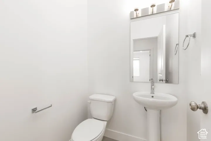 Pedestal sink with chrome faucet, mirror with overhead vanity lighting, and white toilet