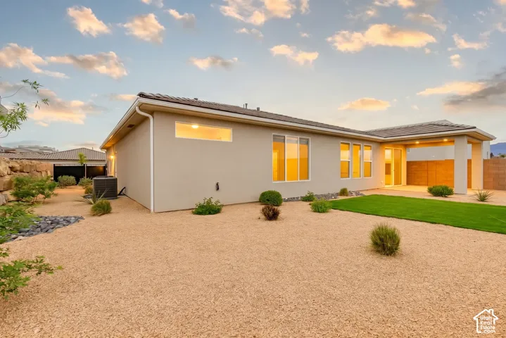 Stucco exterior with a covered patio, multiple windows, and a landscaped yard featuring gravel, artificial turf, and low-maintenance plantings