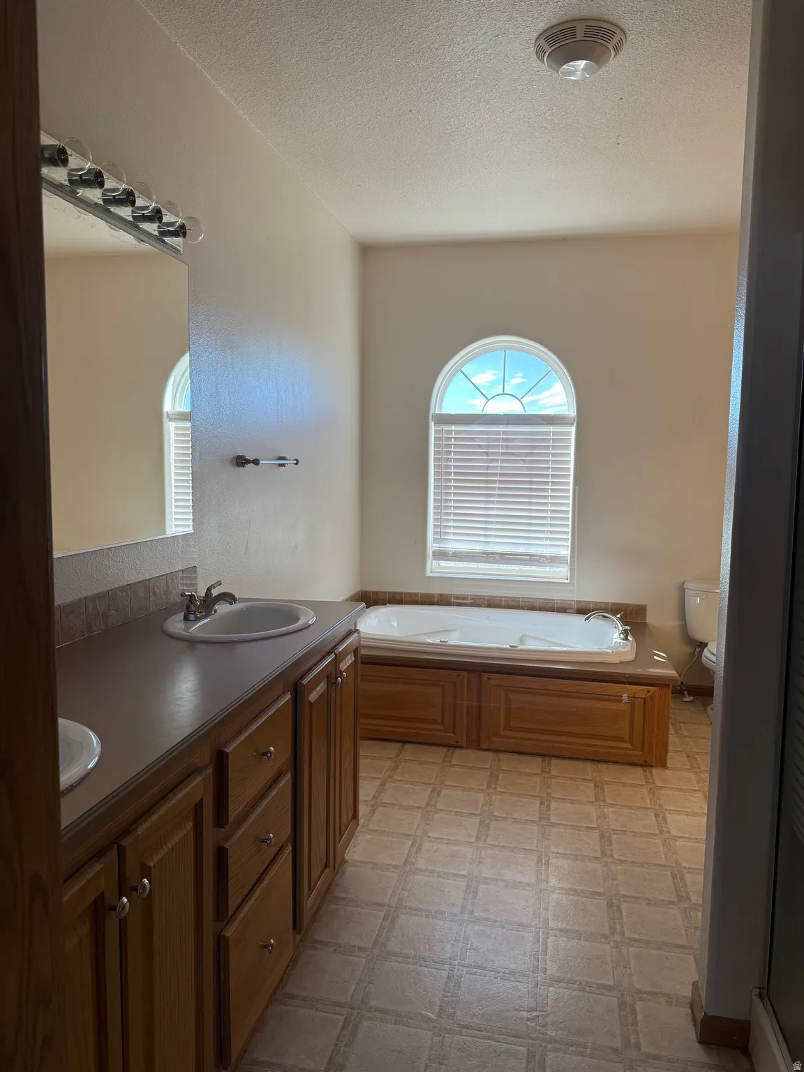 Bathroom featuring double vanity, a bath, light flooring, and a textured ceiling