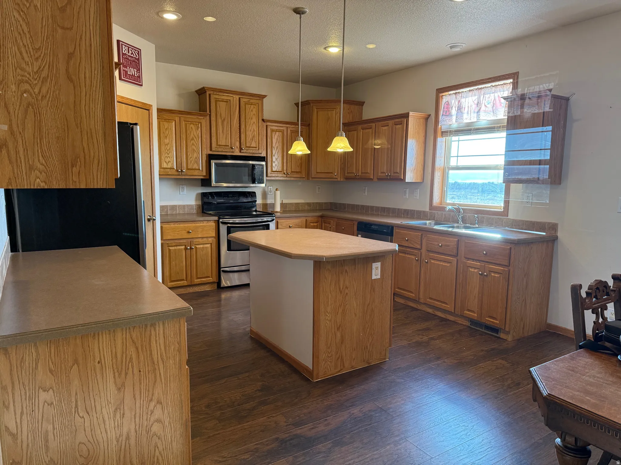 Kitchen featuring stainless steel appliances, wood finish cabinets, a center island, dark wood finished floors, and a textured ceiling