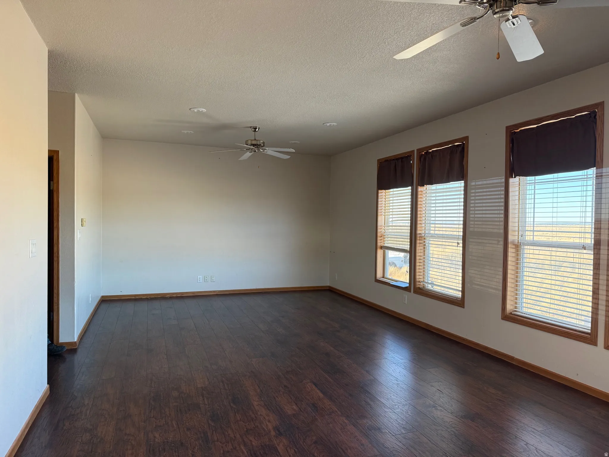 Spare room featuring ceiling fan, dark wood finished floors, and a textured ceiling