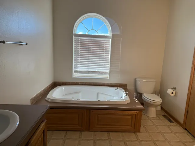 Full bath featuring a whirlpool tub, vanity, and light floors