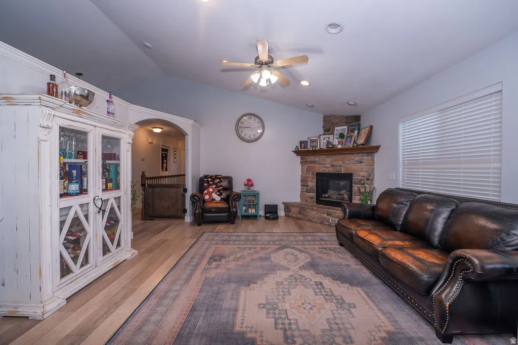 Living area featuring lofted ceiling, a ceiling fan, wood finished floors, a stone fireplace, and arched walkways