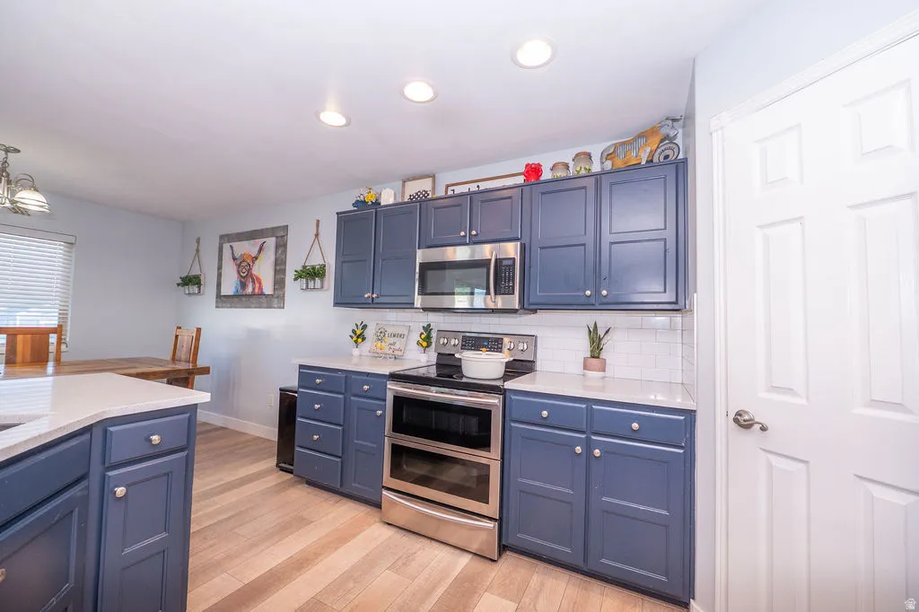 Kitchen featuring stainless steel appliances, blue cabinets, light wood-type flooring, and hanging light fixtures