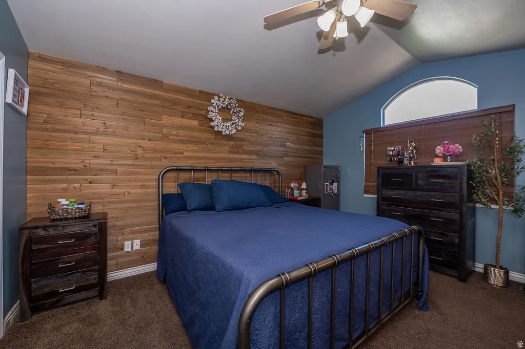 Bedroom featuring wood walls, dark colored carpet, lofted ceiling, ceiling fan, and an accent wall