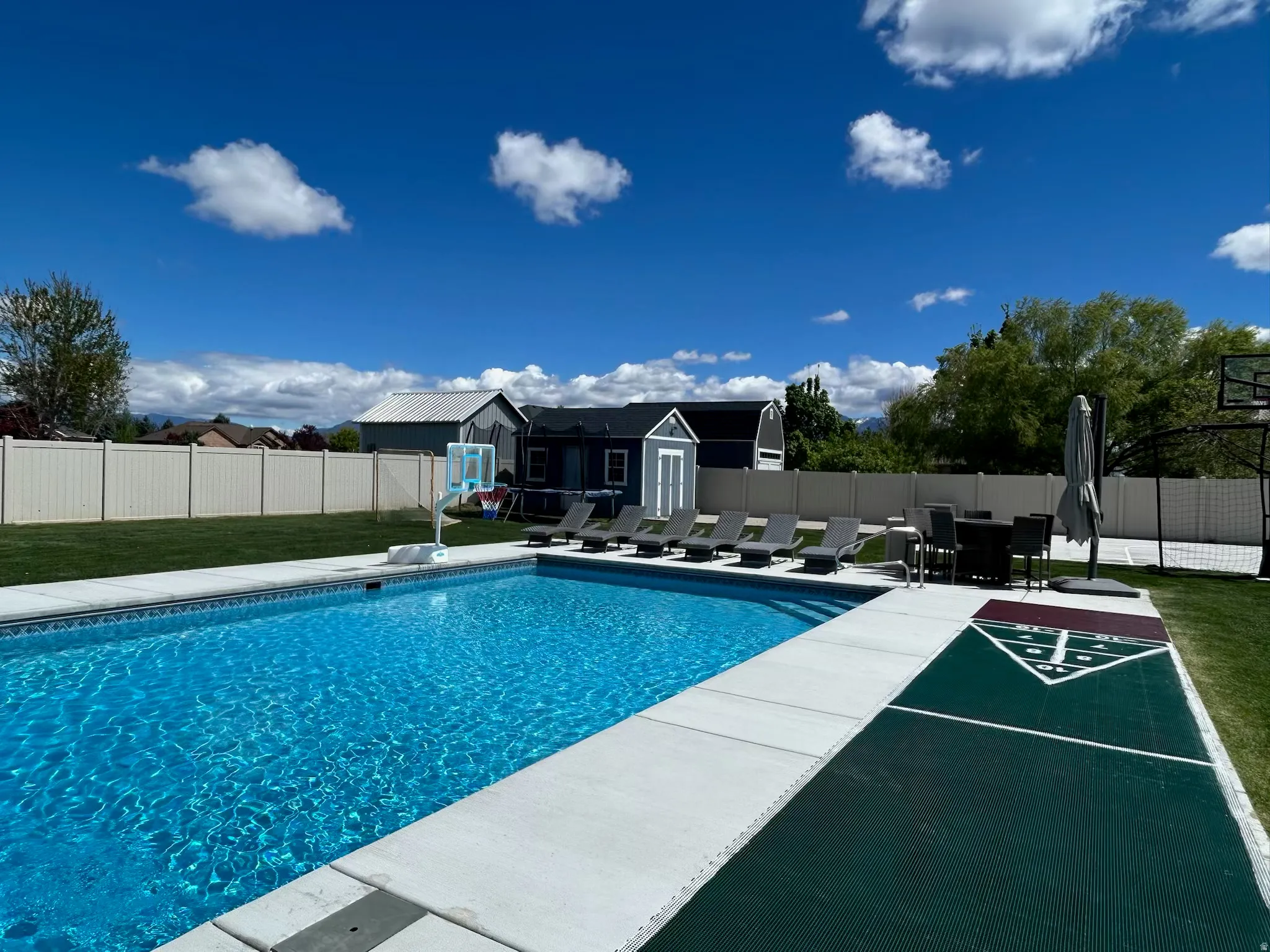 View of swimming pool featuring a fenced backyard, patio surround, an outbuilding, and shuffleboard