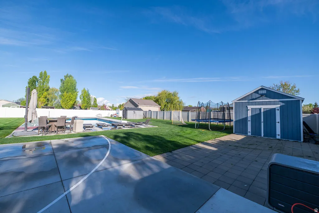 Fenced backyard with a shed, a patio area, outdoor dining area, and a trampoline