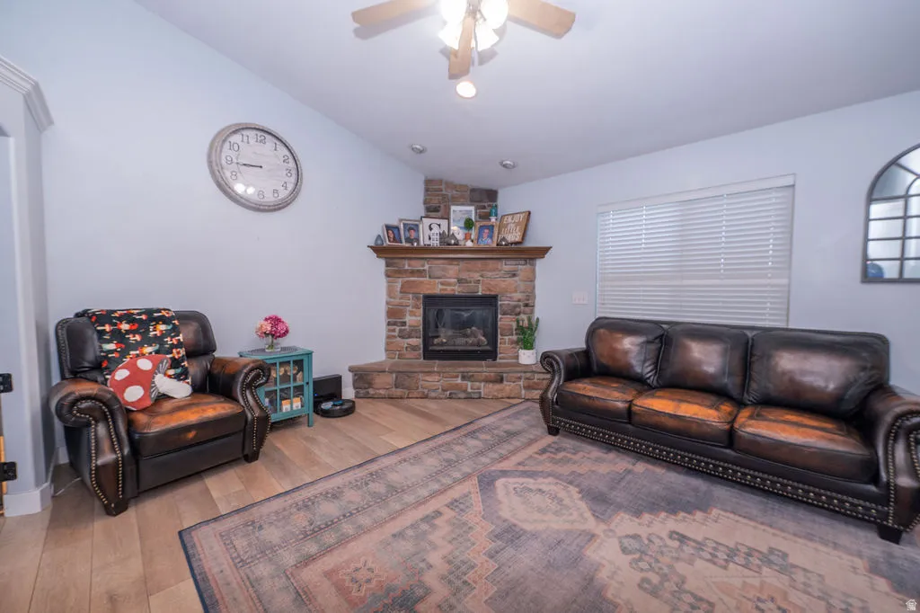 Living area featuring vaulted ceiling, a ceiling fan, light wood finished floors, and a stone fireplace