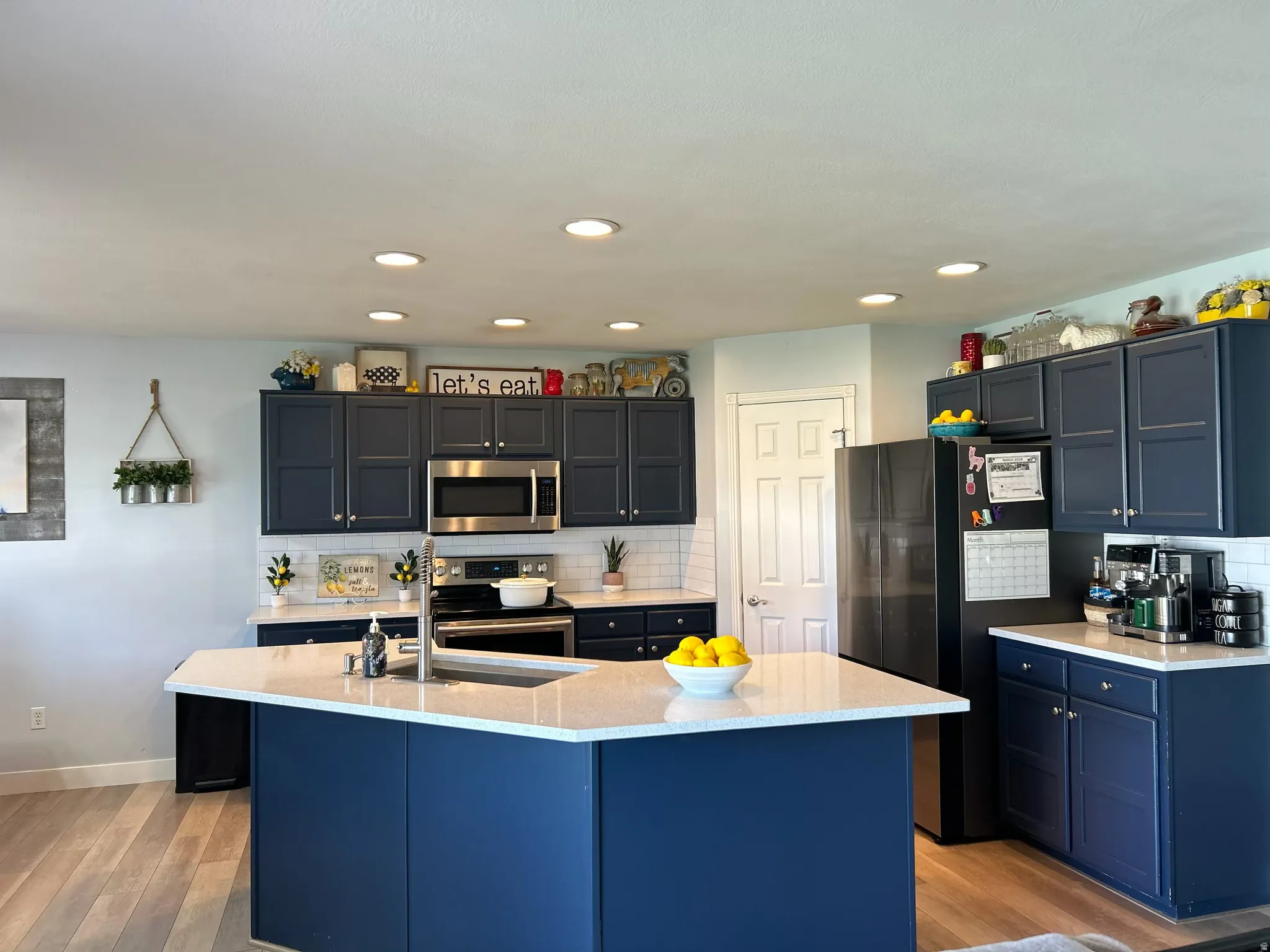 Kitchen featuring stainless steel appliances, light wood-style floors, tasteful backsplash, a center island with sink, and recessed lighting