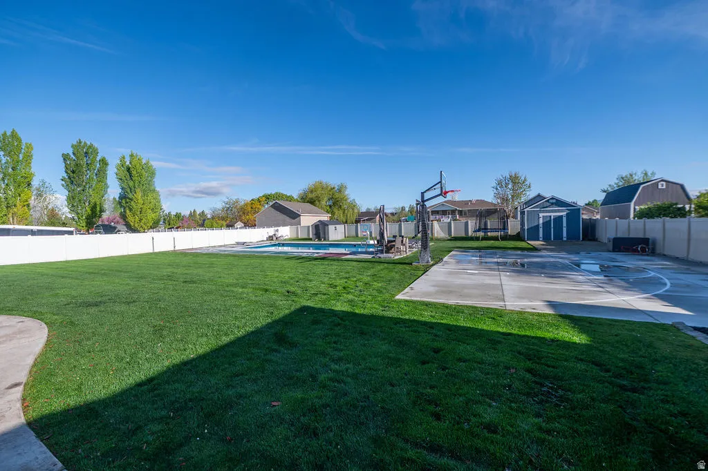 Fenced backyard with a shed, basketball hoop, a residential view, and a patio area