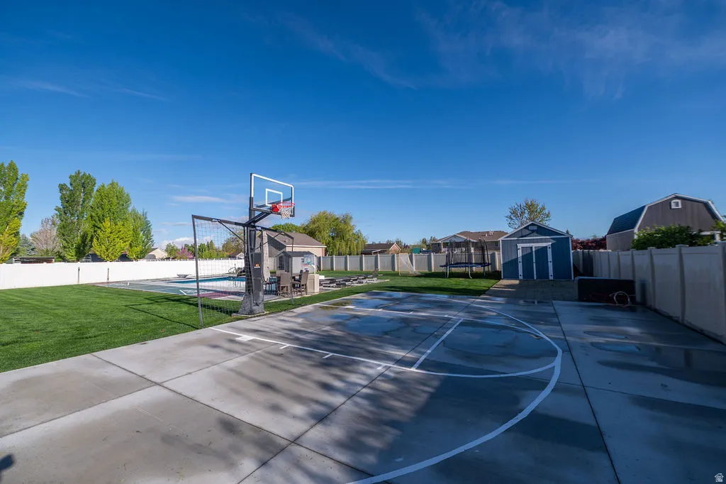View of basketball court featuring a shed, a fenced backyard, basketball court, a trampoline, and a patio area