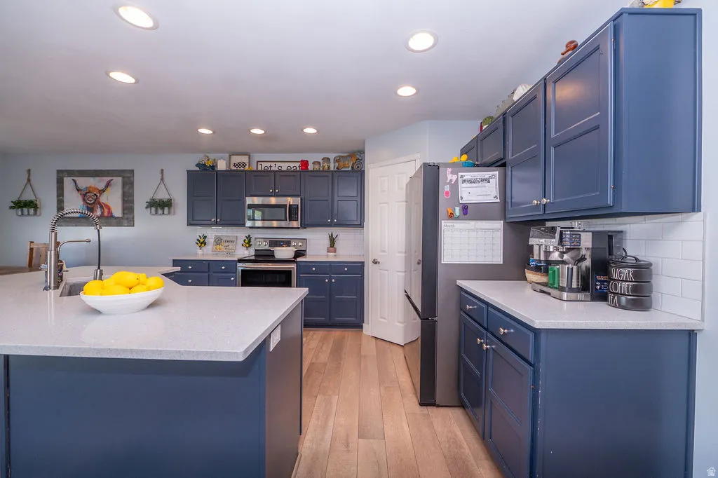 Kitchen with blue cabinetry, stainless steel appliances, light wood finished floors, recessed lighting, and light stone counters