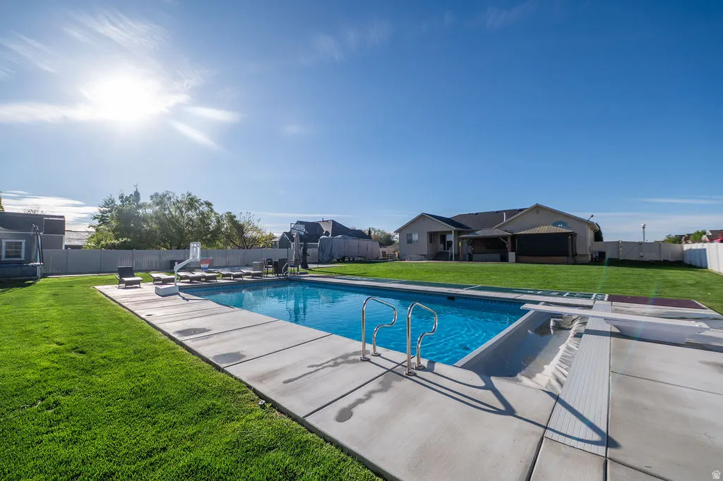 View of pool with patio surround, a diving board, and a fenced backyard
