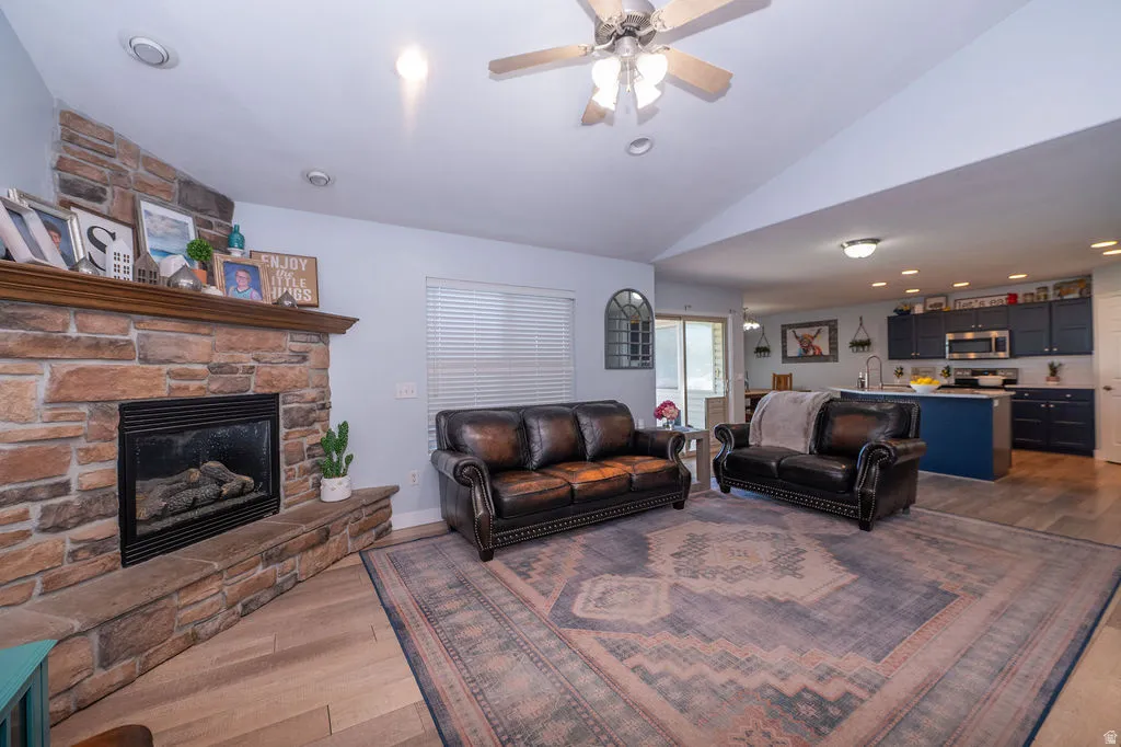 Living room with lofted ceiling, dark wood-type flooring, ceiling fan, recessed lighting, and a fireplace