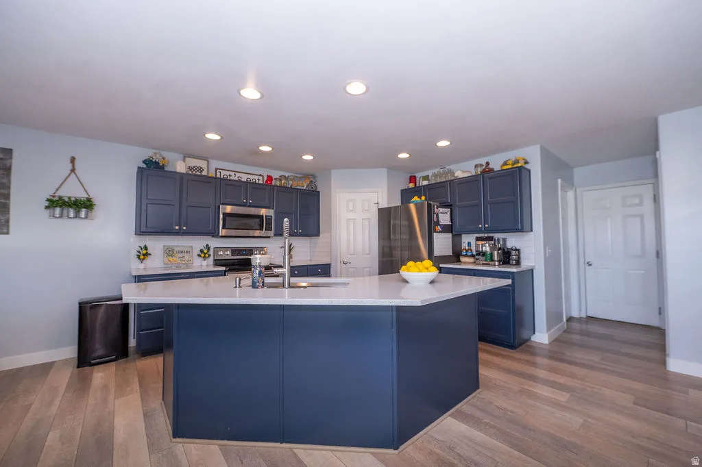 Kitchen with tasteful backsplash, stainless steel appliances, an island with sink, dark wood-style floors, and recessed lighting