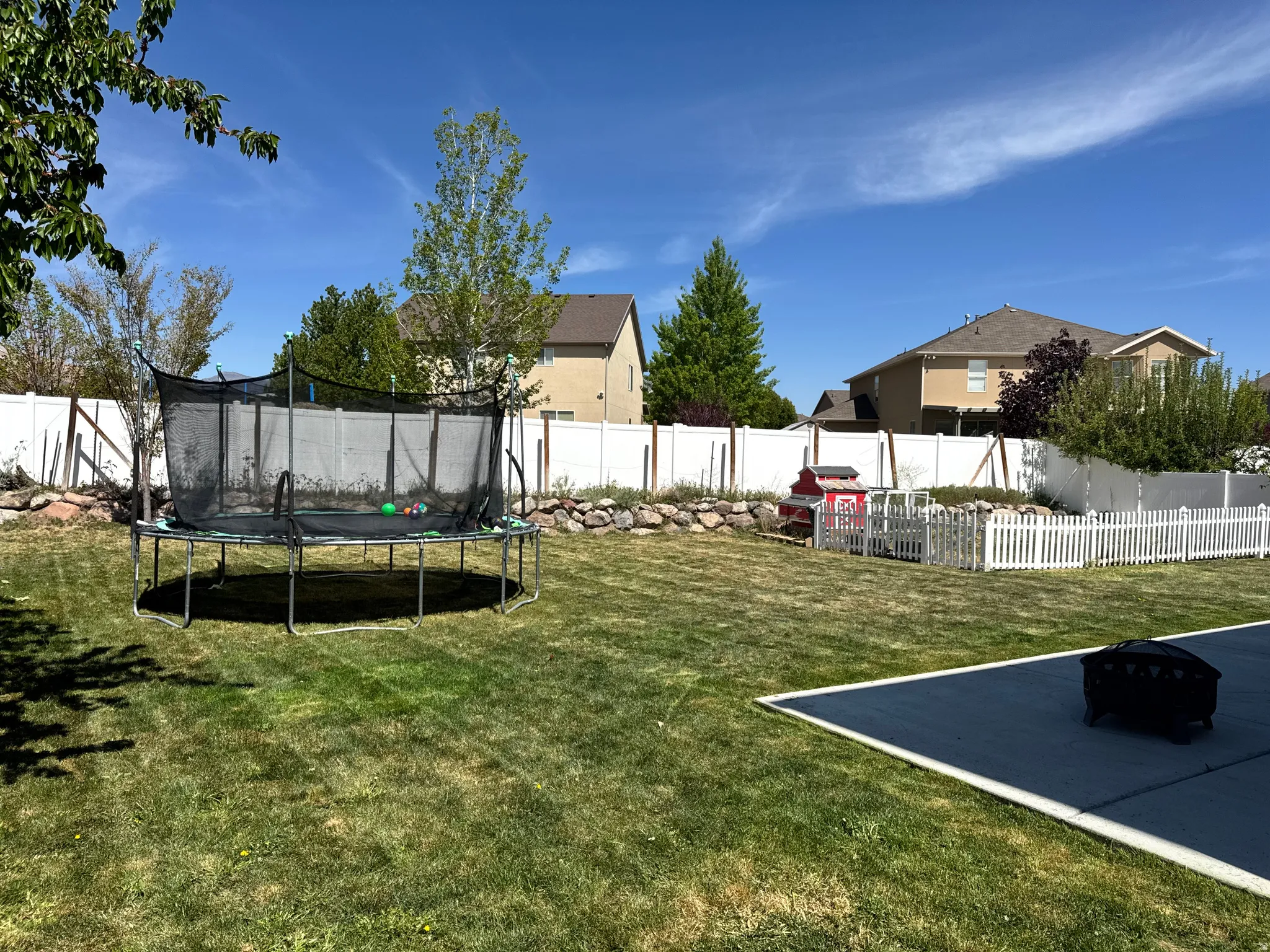 Fenced backyard with a trampoline and a fire pit