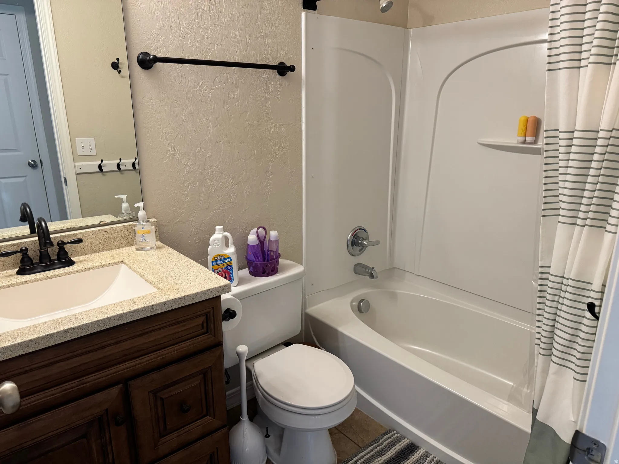 Full bathroom with a textured wall, vanity, and shower / bathtub combination with curtain