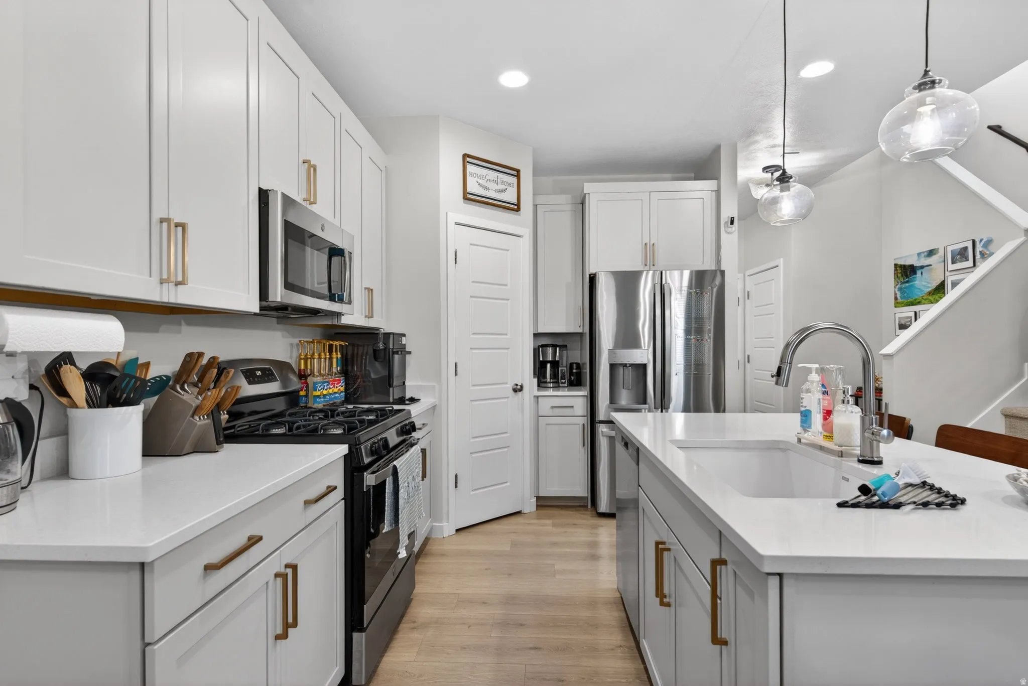 Kitchen with stainless steel appliances, a center island with sink, light wood-type flooring, and light stone countertops