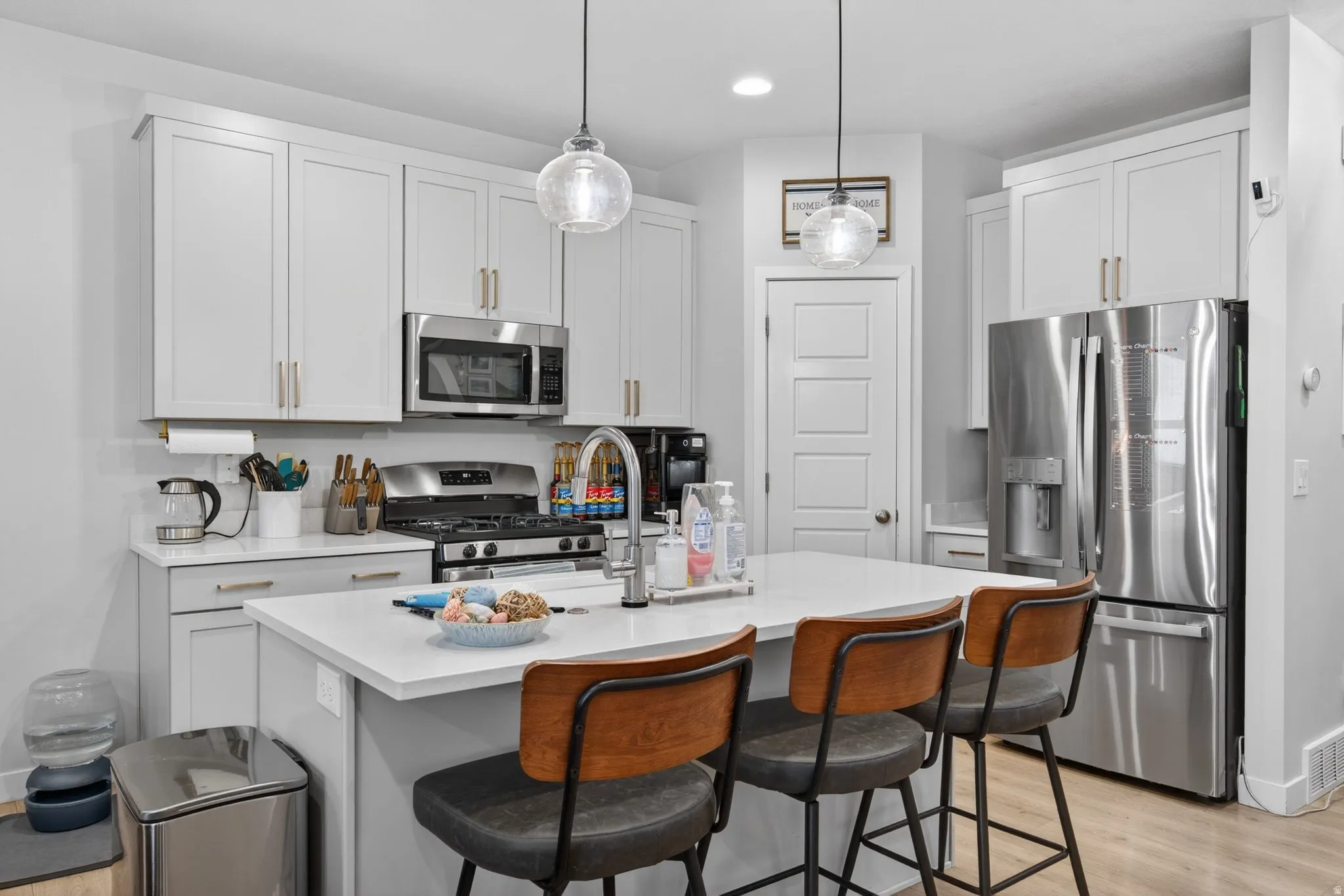 Kitchen featuring stainless steel appliances, a breakfast bar area, light wood finished floors, a kitchen island with sink, and decorative light fixtures
