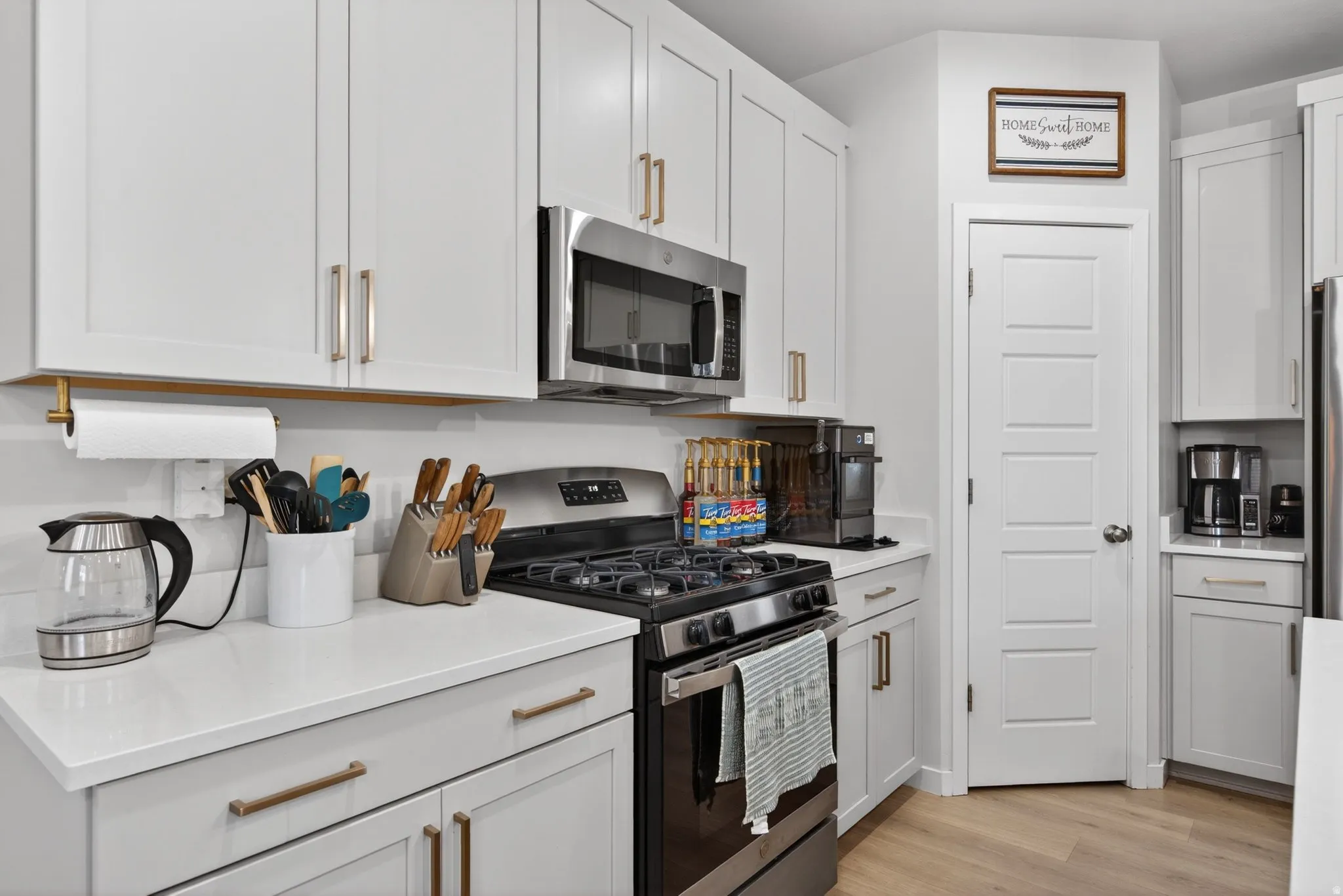 Kitchen featuring stainless steel appliances, light wood-style floors, white cabinets, and light stone countertops