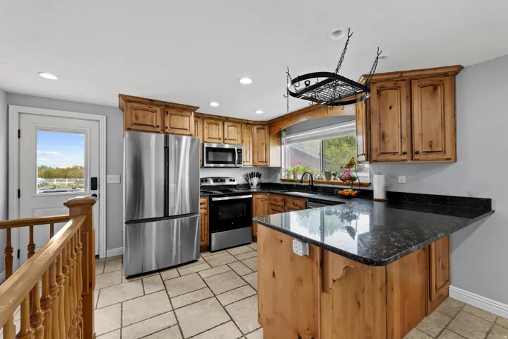 Kitchen with dark stone counters, stainless steel appliances, wood finish cabinetry, a peninsula, and recessed lighting
