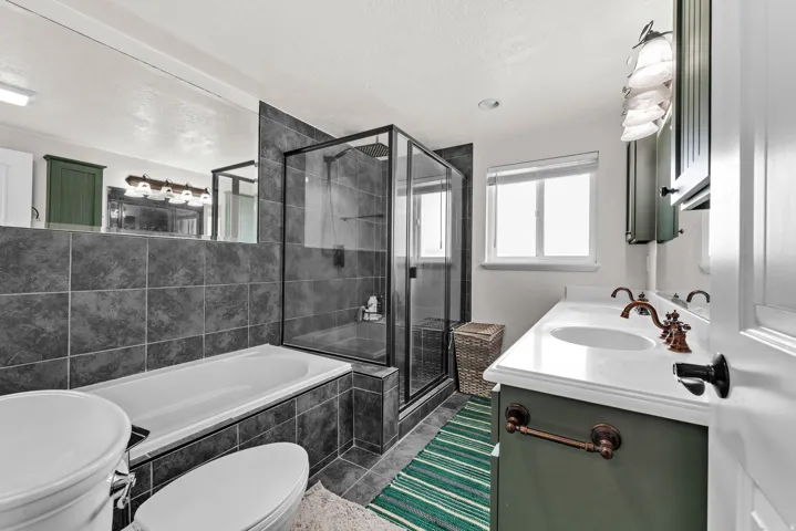 Bathroom with double vanity, a stall shower, a bath, a textured ceiling, and dark tile patterned floors