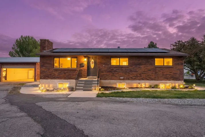 Ranch-style home featuring brick siding, roof mounted solar panels, and a chimney