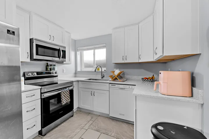 Kitchen featuring stainless steel appliances, white cabinetry, and light stone countertops