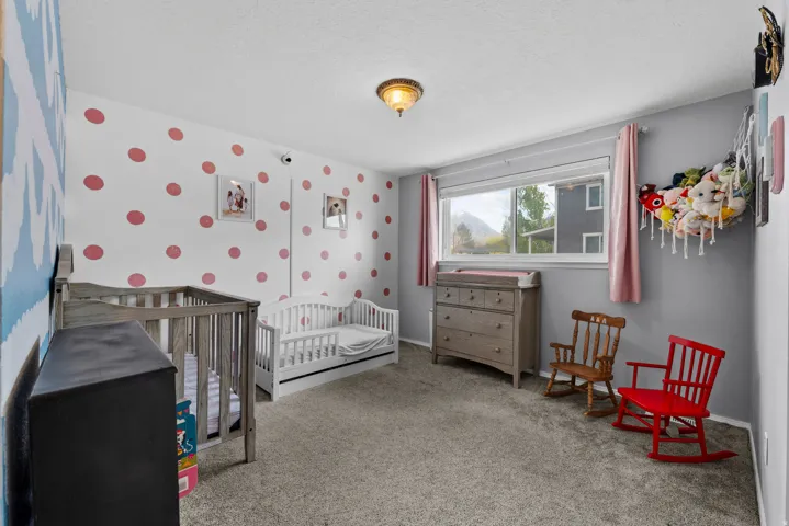 Bedroom featuring wallpapered walls, light colored carpet, a nursery area, and a textured ceiling