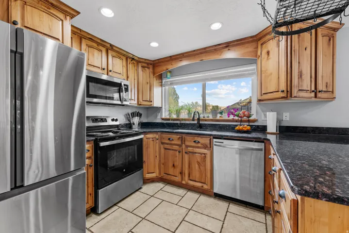 Kitchen with stainless steel appliances, dark stone counters, recessed lighting, wood finish cabinets, and light tile patterned floors