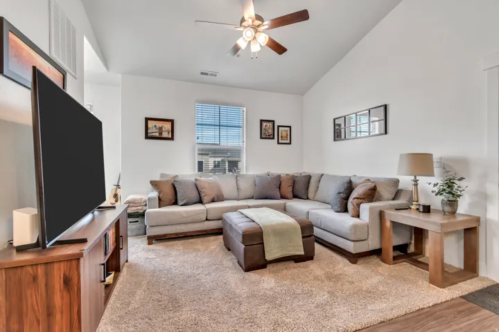 Living room with ceiling fan, vaulted ceiling, and light carpet