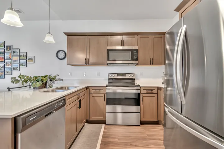 Kitchen featuring stainless steel appliances, a peninsula, light stone countertops, decorative light fixtures, and light wood-style floors