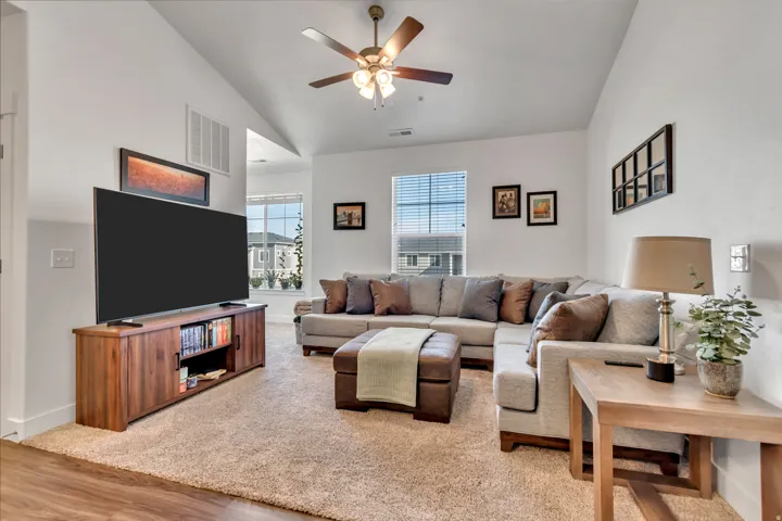 Living room featuring vaulted ceiling, a ceiling fan, light colored carpet, and light wood-type flooring