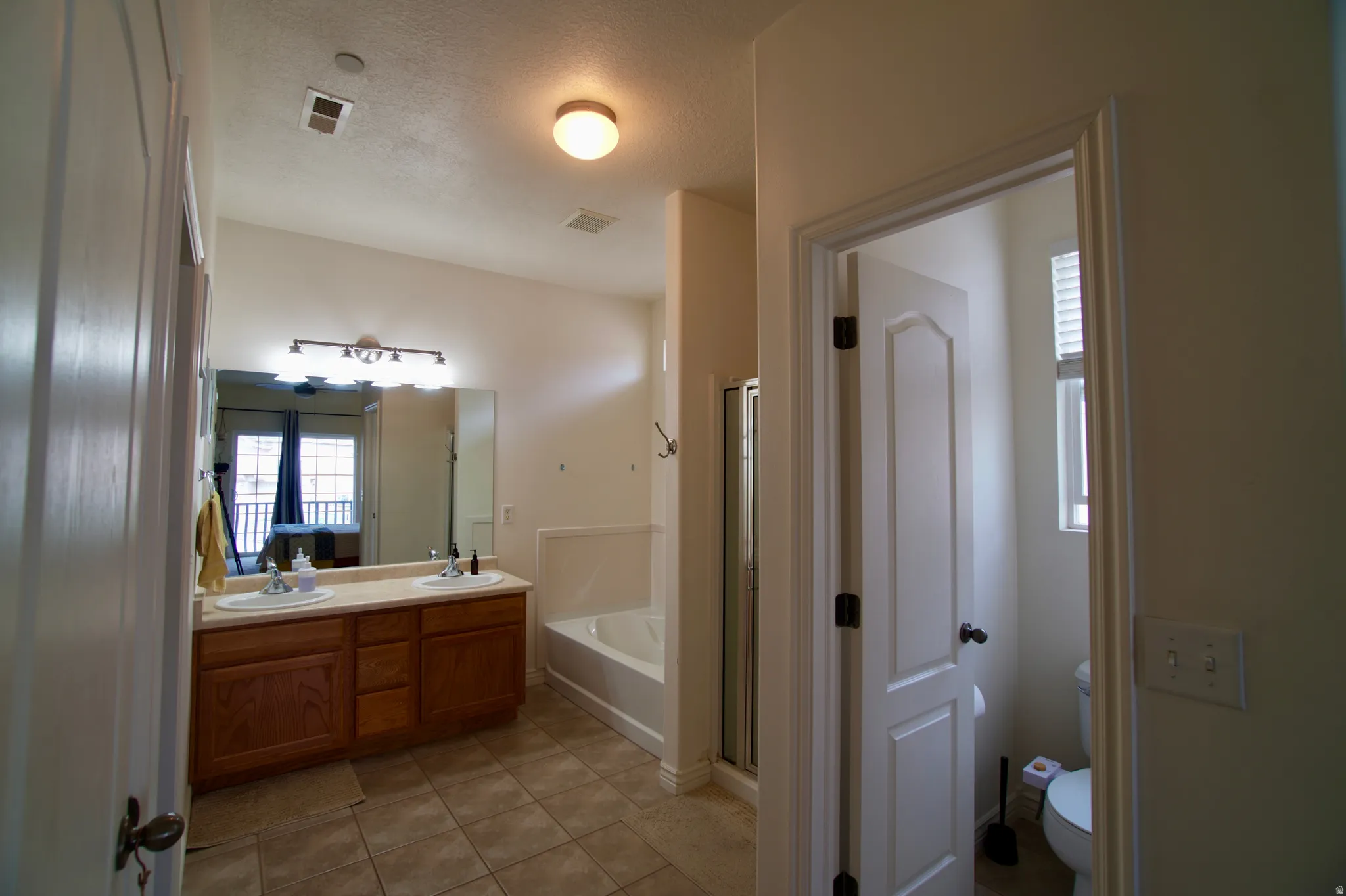 Bathroom featuring double vanity, a stall shower, light tile patterned flooring, a textured ceiling, and a garden tub