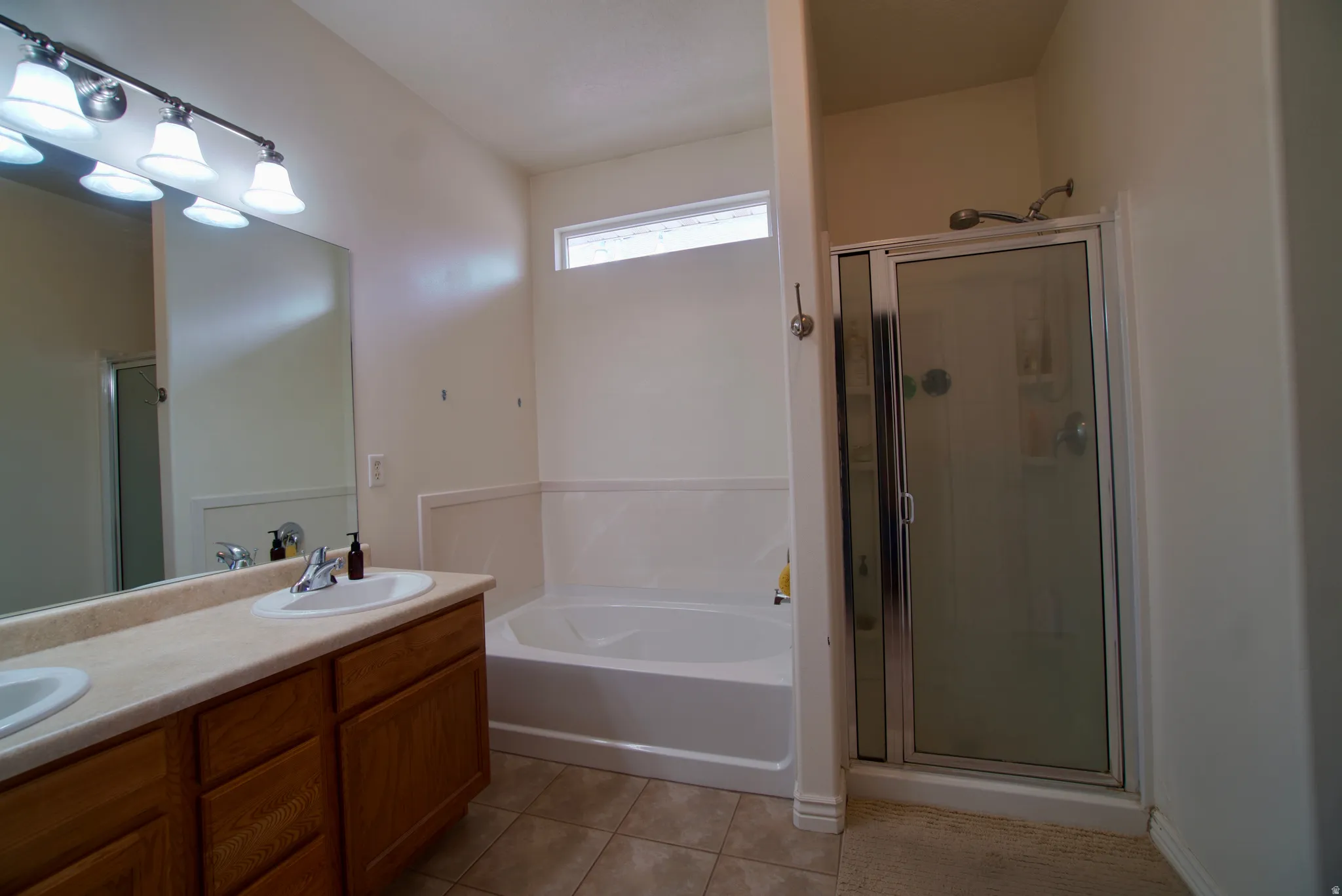 Full bathroom with double vanity, a stall shower, a garden tub, and light tile patterned floors