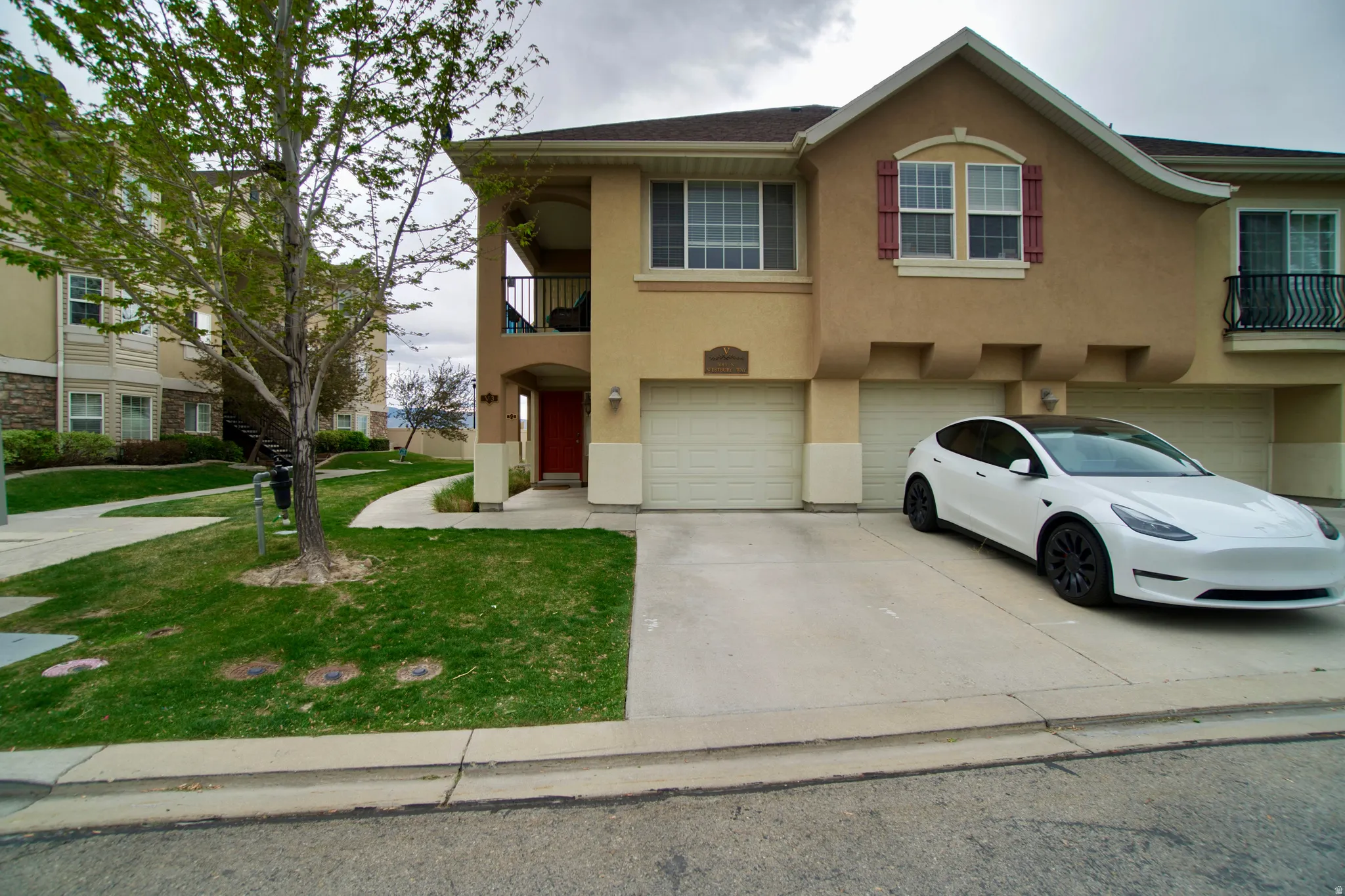 View of front of home featuring a balcony, stucco siding, a garage, driveway, and a front yard