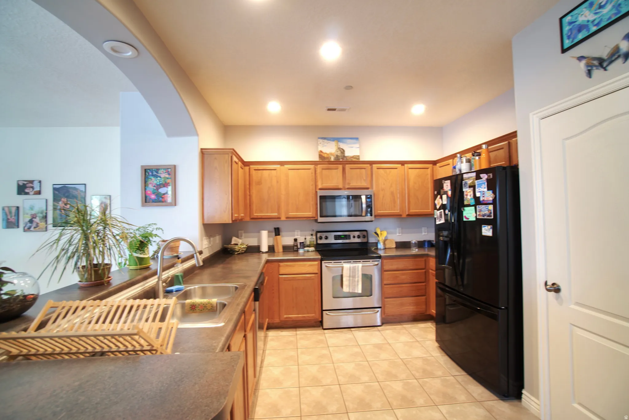 Kitchen with stainless steel appliances, wood finish cabinets, dark countertops, light tile patterned flooring, and recessed lighting