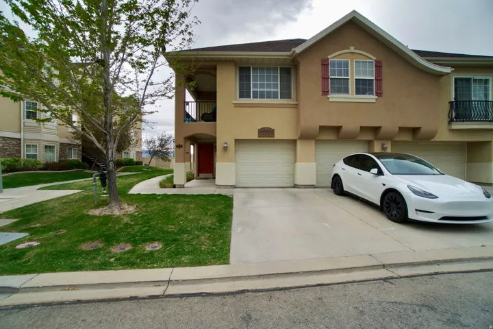 View of front of home featuring a balcony, stucco siding, a garage, driveway, and a front yard