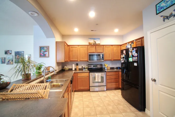 Kitchen with stainless steel appliances, wood finish cabinets, dark countertops, light tile patterned flooring, and recessed lighting