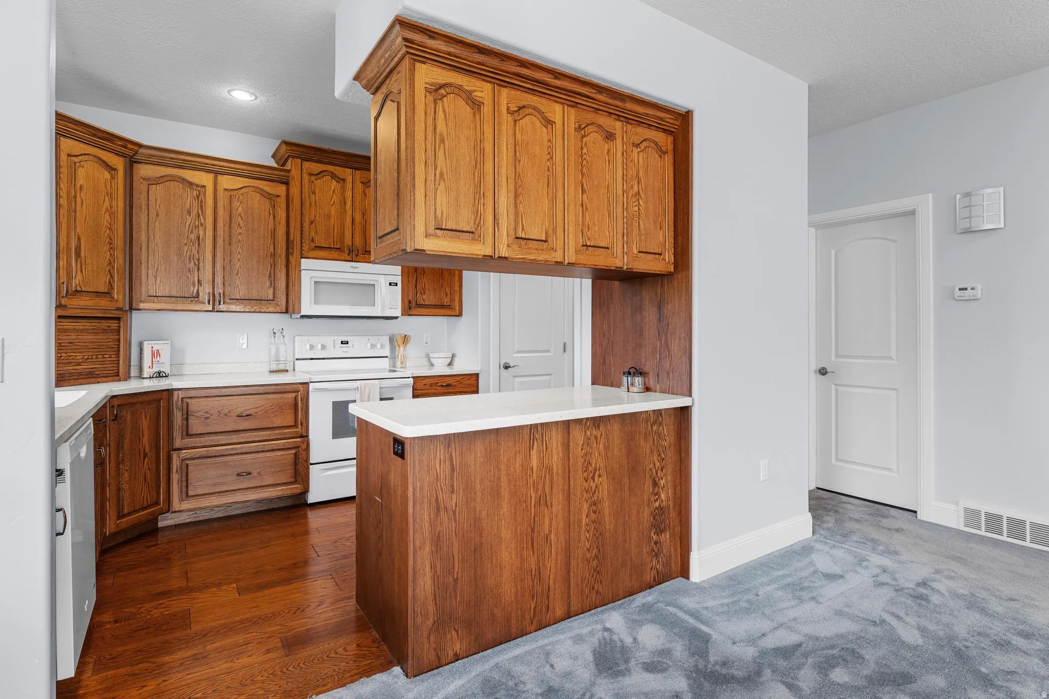 Kitchen with wood finish cabinets, light countertops, white appliances, and a peninsula