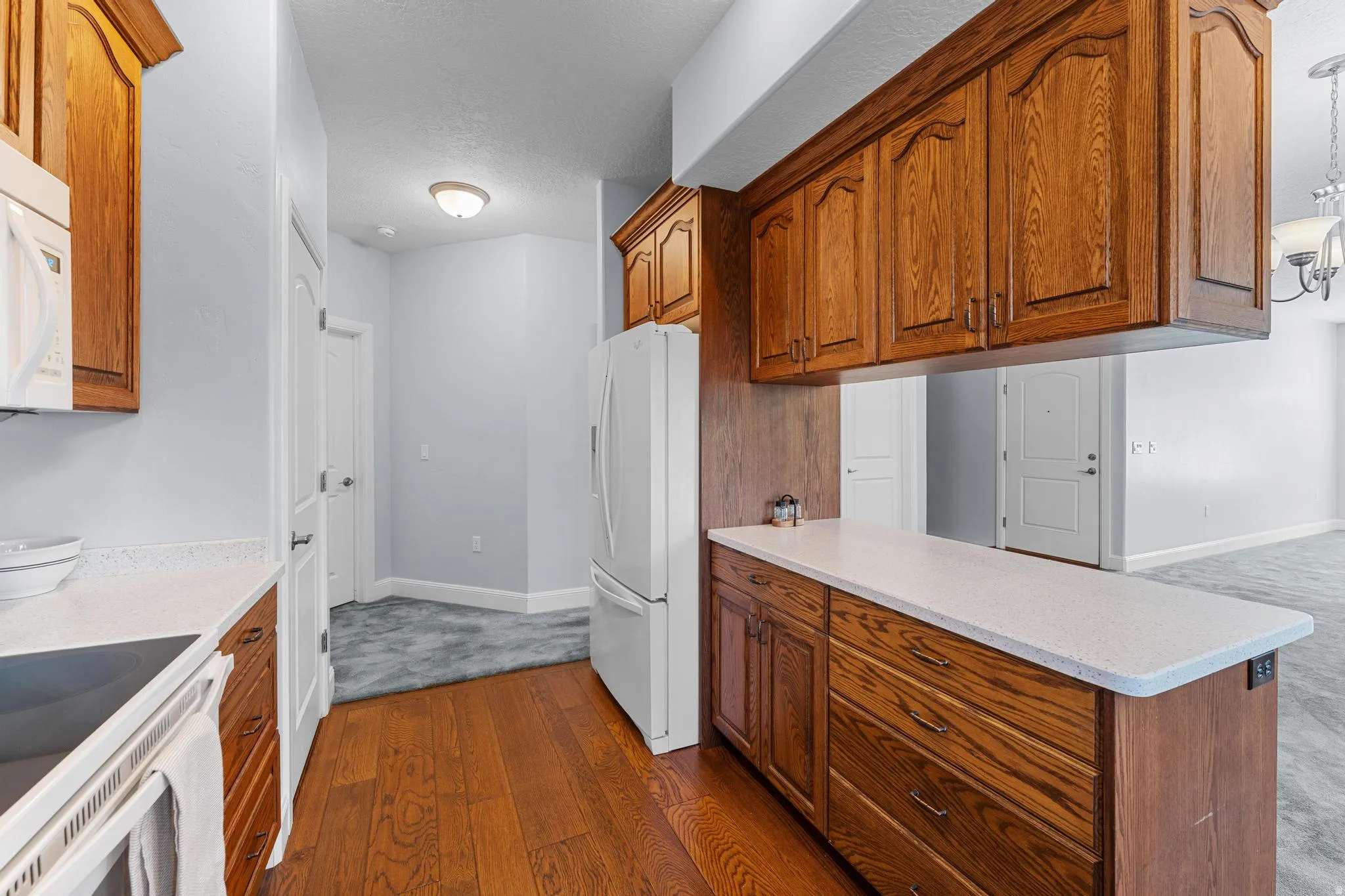 Kitchen with white appliances, light stone countertops, wood finish cabinets, a peninsula, and dark wood finished floors