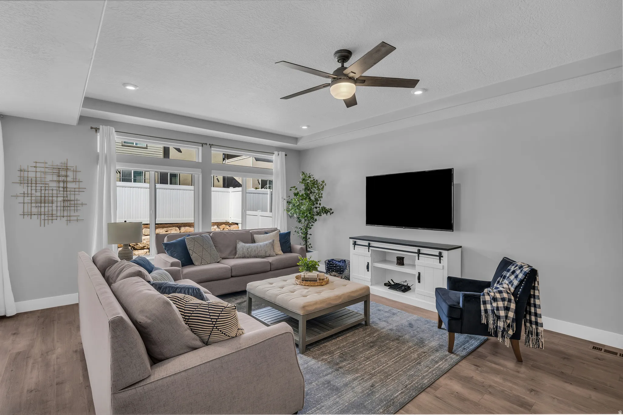 Living area with wood finished floors, ceiling fan, a raised ceiling, and a textured ceiling