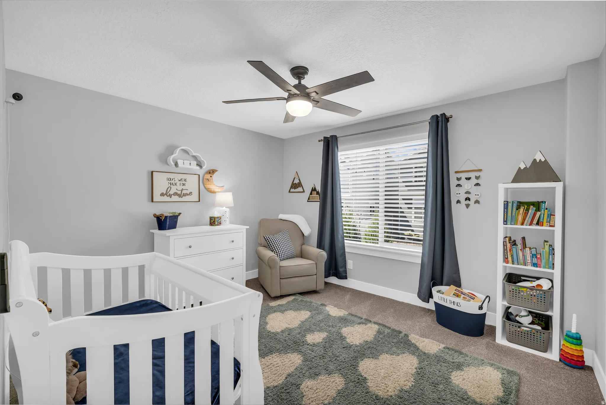 Carpeted bedroom with a crib and a ceiling fan