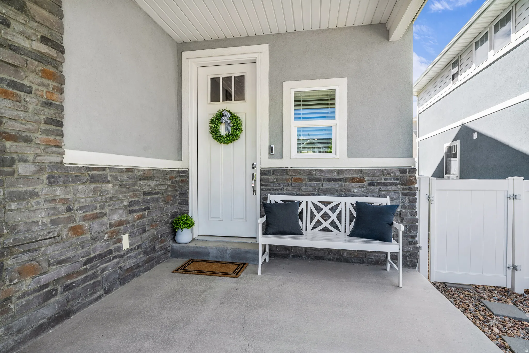 View of exterior entry featuring stone siding, a gate, covered porch, and stucco siding