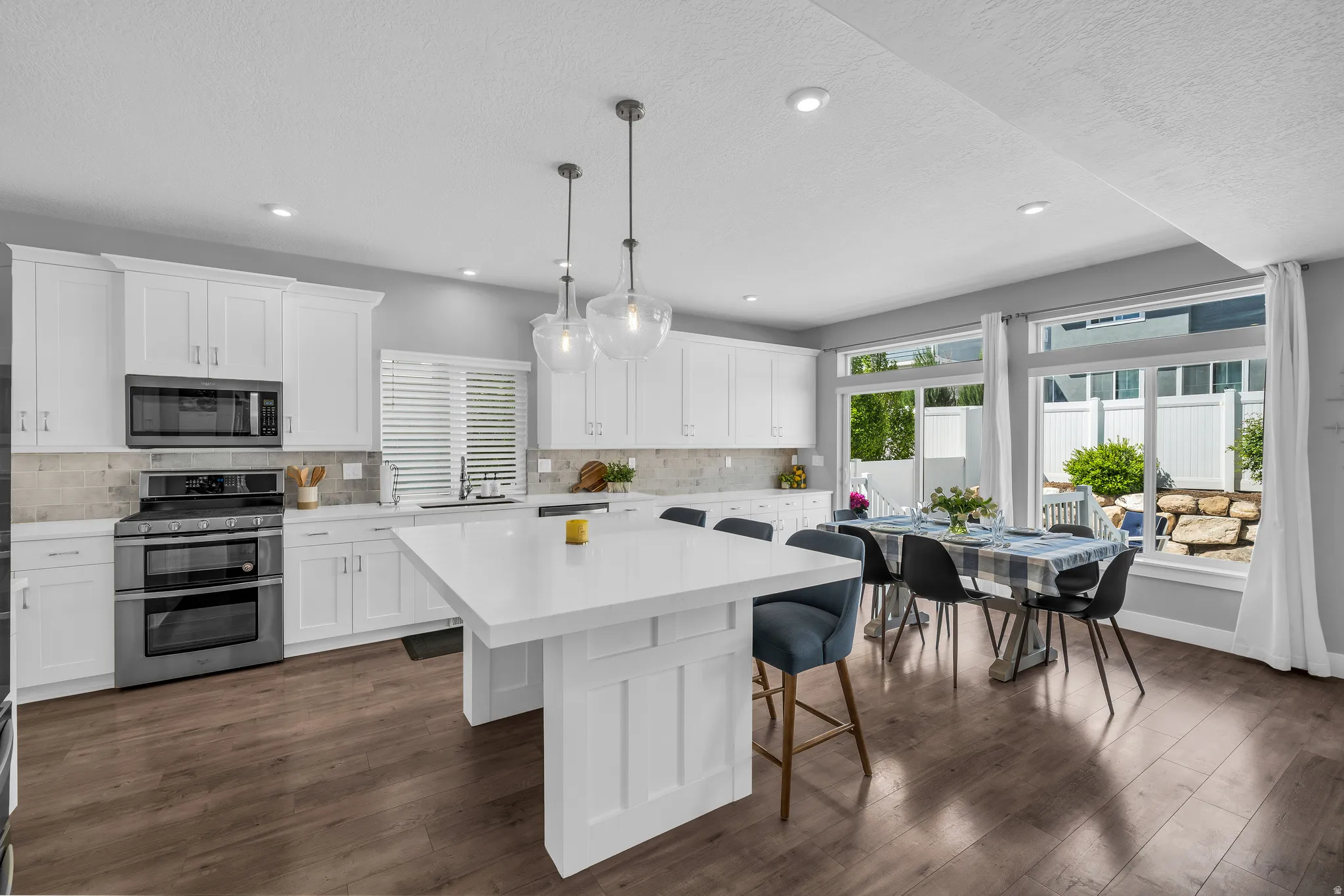 Kitchen with stainless steel appliances, a kitchen breakfast bar, white cabinetry, decorative light fixtures, and a textured ceiling