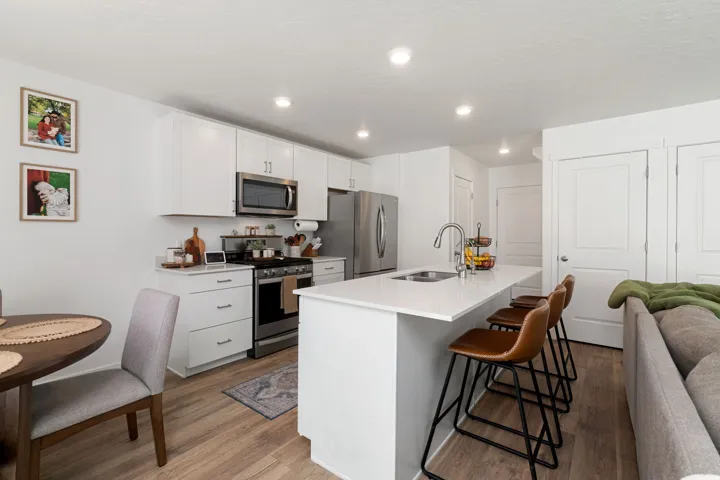 Kitchen featuring stainless steel appliances, a center island with sink, a breakfast bar area, white cabinets, and light wood-style flooring