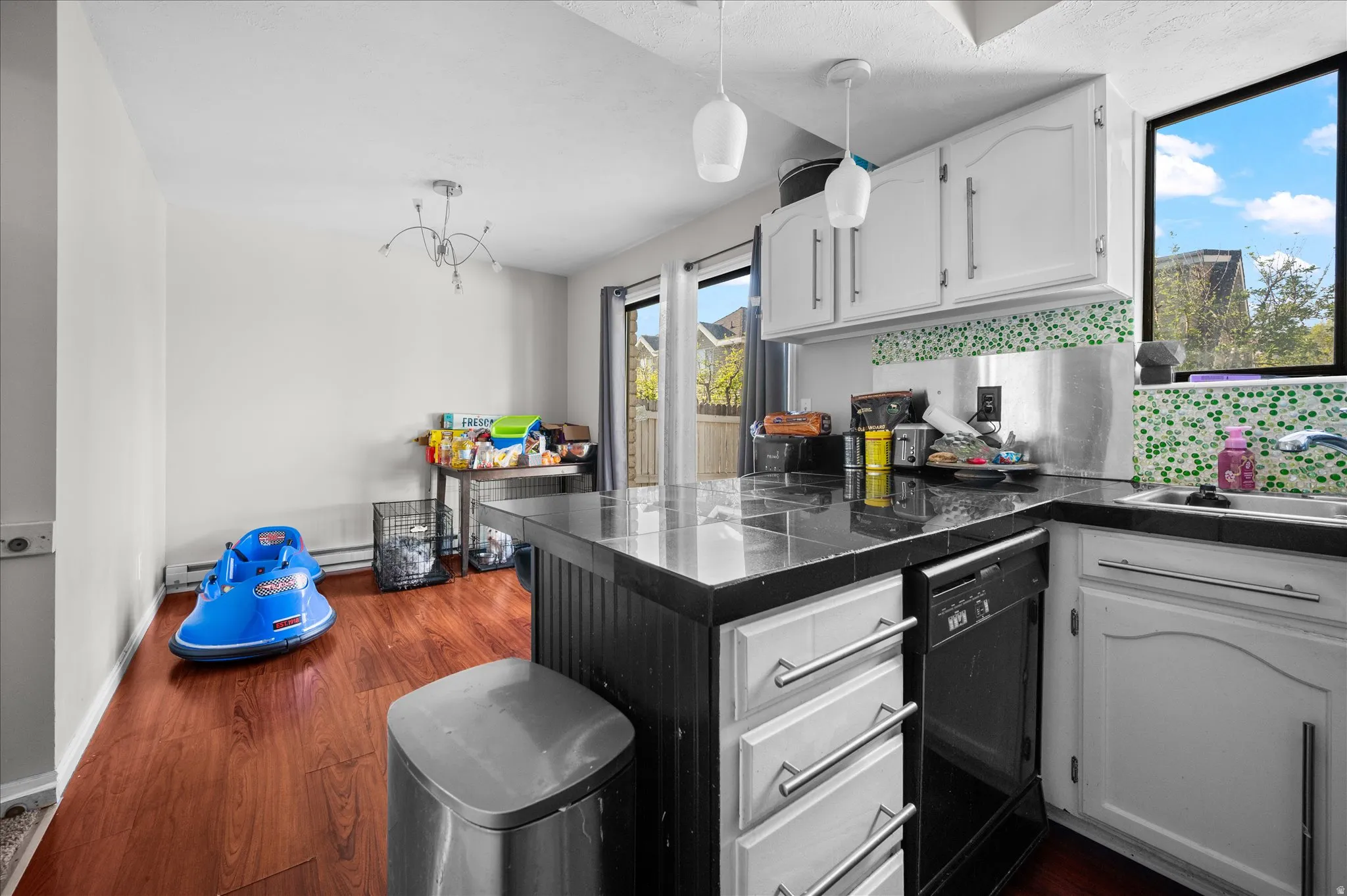 Kitchen featuring tile countertops, white cabinets, decorative light fixtures, and a peninsula